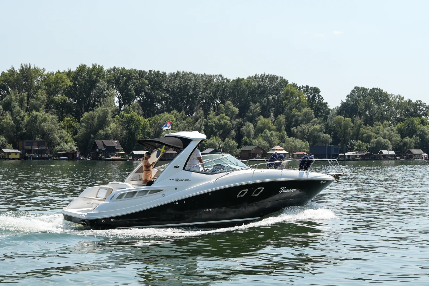 Sea Ray 335 Timescape u vožnji Dunavom sa pogledom na obalu i kućice na vodi.